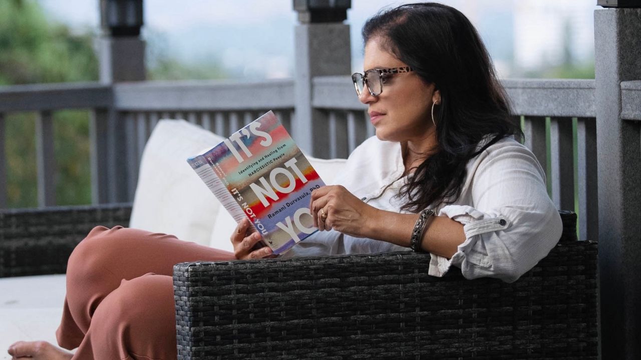 Dr Ramani reading her book, It's Not You on a lounge chait outside